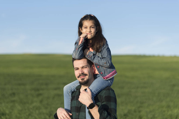 Modern father with daughter on shoulders in spring field - Foto, Imagem