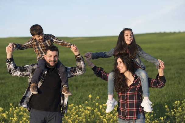 Four happy family members, playing children on parents shoulders - Fotó, kép