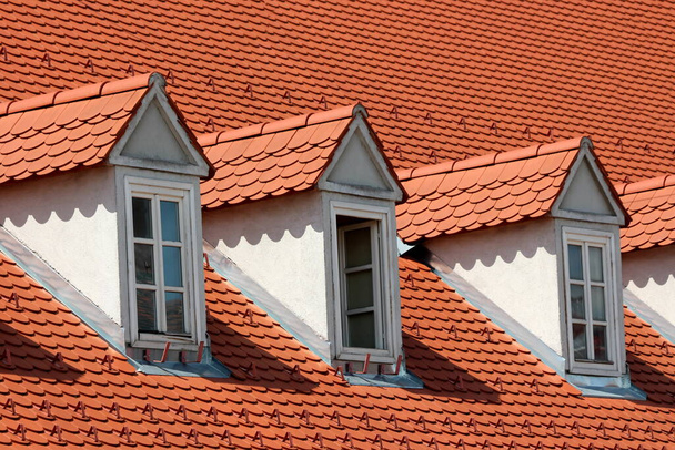 Felújított régi stílusú tetőablakok sora, amelyeket új piros tetőcserepek és hóvédők borítanak a külvárosi családi ház tetejére a város régi részén - Fotó, kép