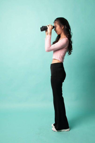 Full body of young Asian woman with binoculars on cyan background - Фото, зображення