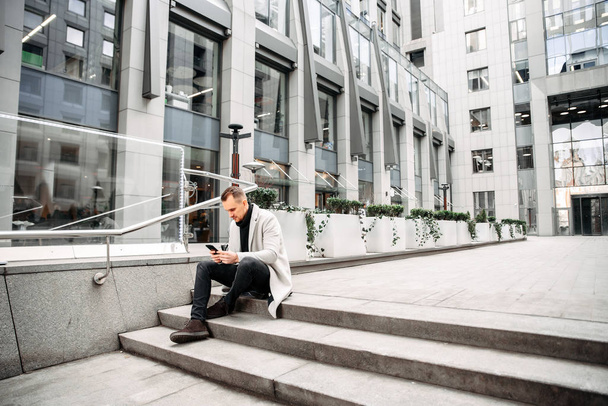 Attractive guy in casual coat sits on the steps - 写真・画像