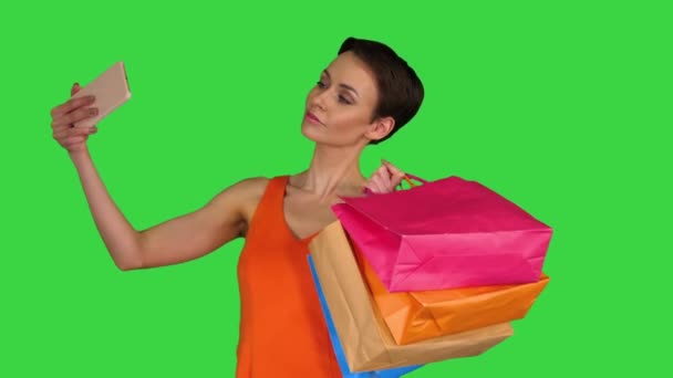 Vonzó fiatal nő kezében különböző üres bevásárló táskák, hogy szelfi egy zöld képernyőn, Chroma Key. - Felvétel, videó