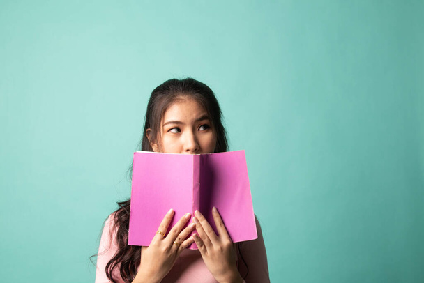 Young Asian woman with a book cover her face on cyan background - Photo, Image