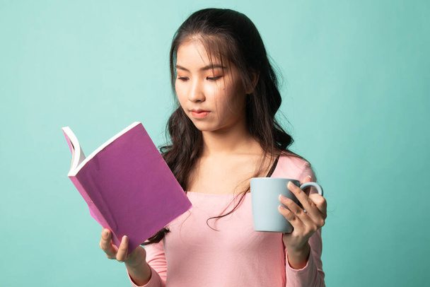 Young Asian woman with a book and cup of coffee on cyan background - 写真・画像