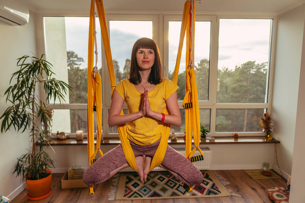 Fly Yoga. Woman doing yoga exercises on a hammock in an apartment. - Foto, Imagen