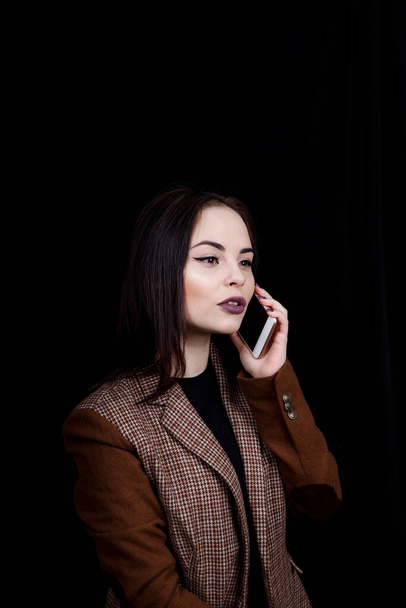 Joyful and successful young woman fashion blogger is emotionally talking on phone. Beautiful young woman in casual grey jacket is holding smartphone - Фото, зображення