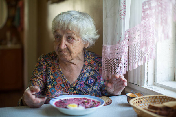 An old woman sitting at the table eat soup. - Photo, Image