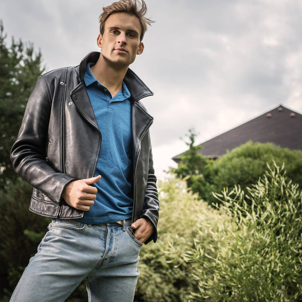 Young handsome man in classic leather jacket pose in summer garden. - Foto, imagen
