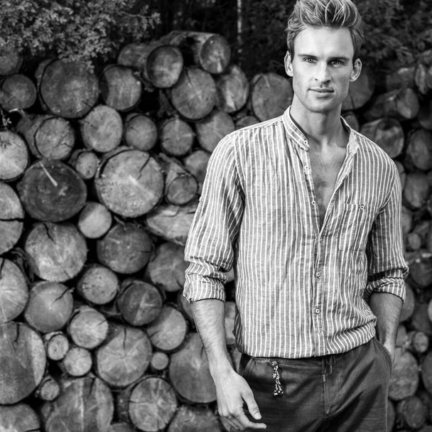 Young handsome man in casual shirt poses near wooden background. Black-white photo. - Photo, image