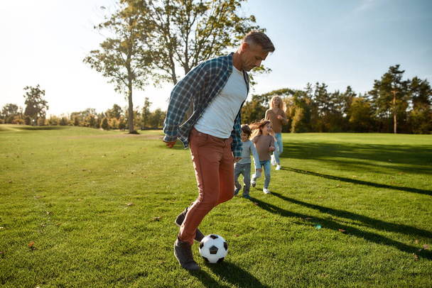 Rakastamme jalkapalloa. Onnellinen perhe leikkii pallolla niityllä
 - Valokuva, kuva