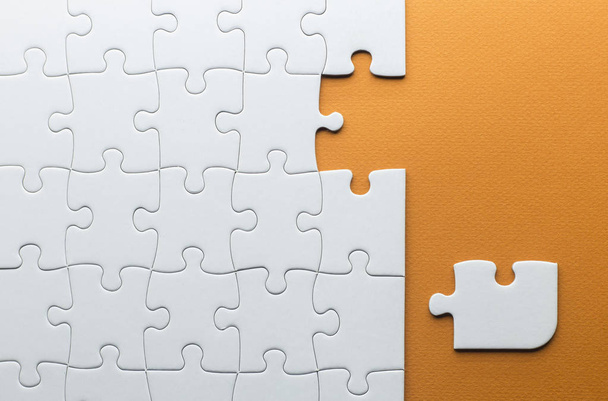 ein Puzzleteil, das nicht zu den anderen passt, weiße Puzzleteile auf orangefarbenem Hintergrund - Foto, Bild