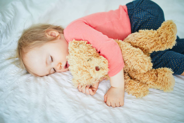 Adorable baby girl sleeping with her favorite toy. Little child having a day nap and hugging a teddy bear. Infant kid resting in nursery - Fotografie, Obrázek