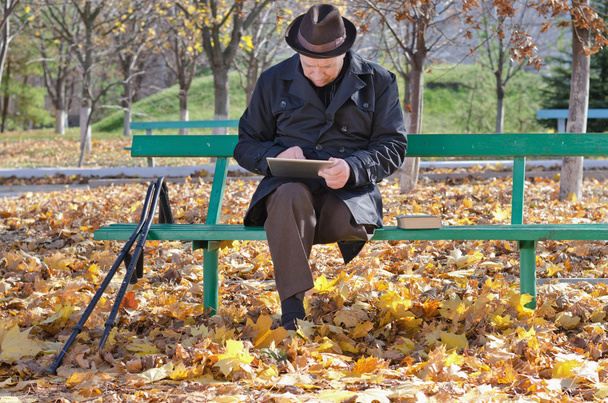 Älterer Mann auf Krücken mit Tablet im Park - Foto, Bild