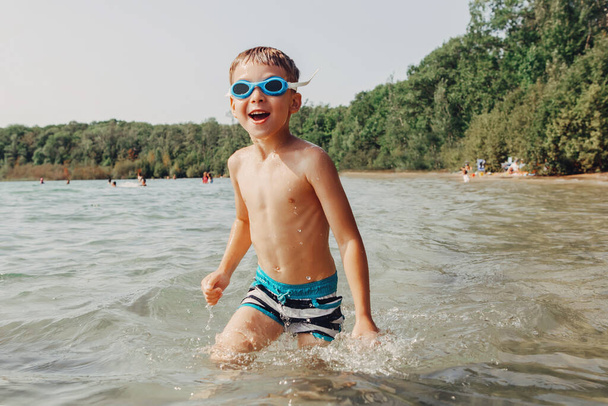 水中ゴーグルで湖で泳ぐかわいい面白い白人の少年。ビーチで水の中で子供ダイビング。本物の生活幸せな子供時代。夏の楽しい屋外季節の活動. - 写真・画像
