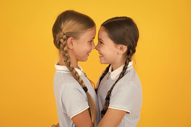Friendly hug. Cute schoolgirls. Girls braided hairstyle. Cheerful schoolgirls yellow background. Little girls playing with cute braids. Beautiful schoolgirls best friends. Back to school concept - Fotó, kép