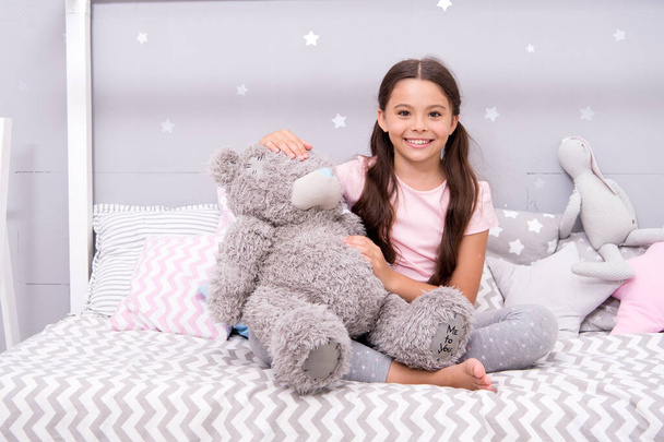 Imaginary interaction. Play games. Favorite toy. Girl child hug teddy bear in her bedroom. Pleasant time in cozy bedroom. Girl kid long hair cute pajamas relax and play plush teddy bear toy. - Foto, afbeelding