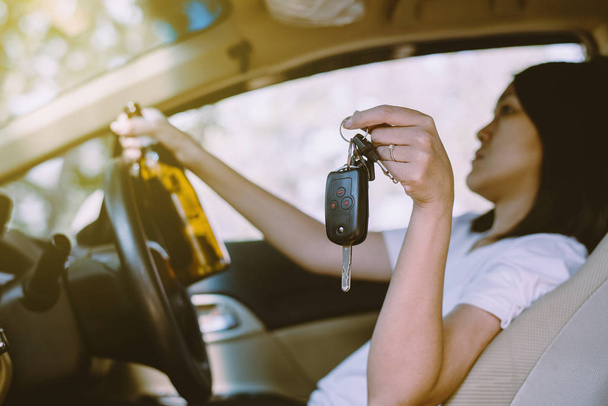 Drunk asian woman holding car key and drinking alcohol while driving car on road,Women drive her car with a bottle of beer,Dangerous driving concept - Fotó, kép