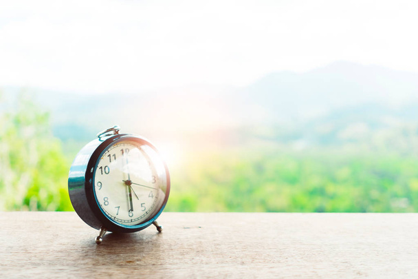 Selective focus of alarm clock on table with nature bokeh mountain background. Time in life concept and morning person. - Photo, Image
