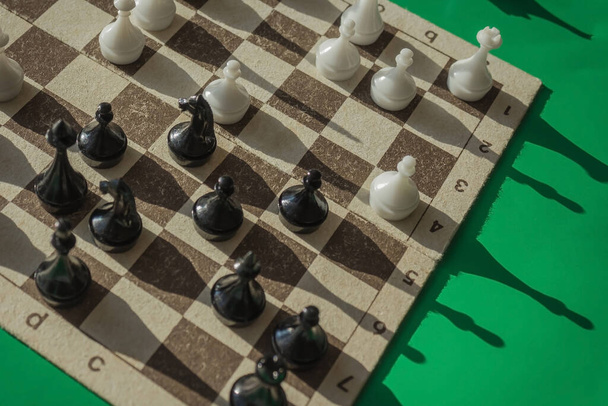 On the chessboard are black and white figures, the game is in full swing. Analysis of the situation, logical thinking. Green background, top view. - Photo, Image