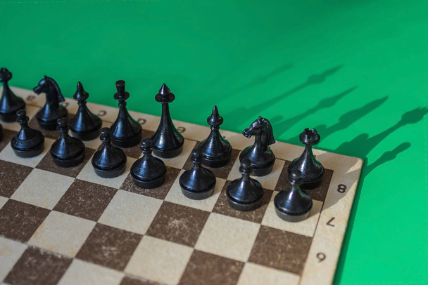 Fekete darabok és gyalogok a sakktáblán, a kezdeti konstrukció. A játék kezdete, a helyzet elemzése. Oldalsó napfény, zöld háttér. - Fotó, kép