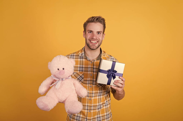 What to buy. happy valentines day. teddy bear plush toy. his favorite holiday. best offer while shopping. macho man teddy bear gift. guy hold present box yellow wall. birthday present surprise - Zdjęcie, obraz