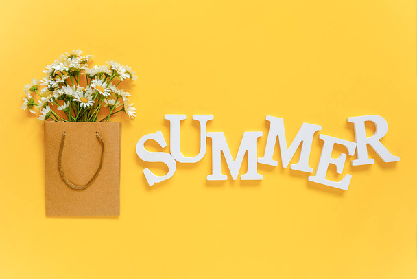 Text SUMMER from white volume letters and field chamomiles flowers in craft package on yellow background. Greeting card Flat Lay Copy space Concept Hello summer, summertime. - Foto, Imagen