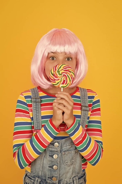 Sweet tooth. Little child hold lollipop candy yellow background. Small girl with rainbow swirl candy on stick. Adorable kid enjoy sugar candy dessert. Best candy shop - Fotó, kép