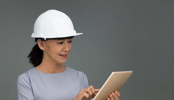 Beautiful Asian Smart Architect Engineer 50s 60s years old woman in white hard hat helmet hold tablet iot, portrait studio lighting gray background copy space, concept aging society woman can do - Foto, imagen