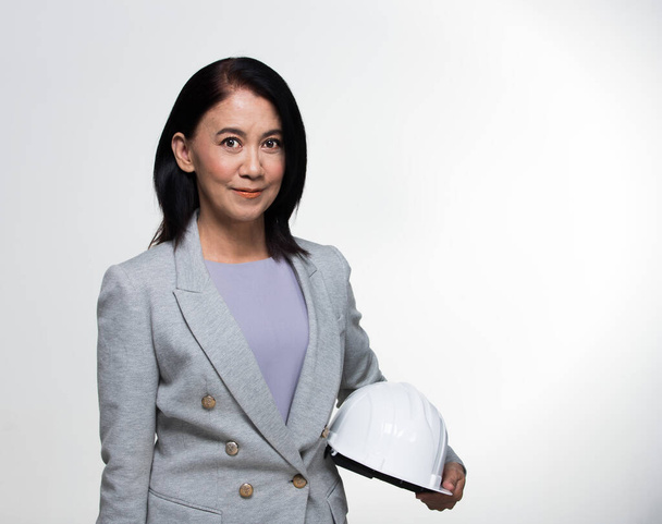Beautiful Asian Smart Architect Engineer 50s 60s years old woman in white hard hat helmet look at camera, portrait studio lighting gray background copy space, concept aging society woman can do - Foto, imagen