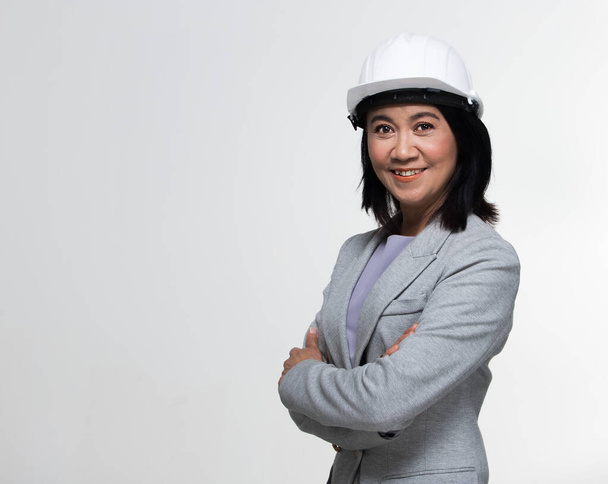 Beautiful Asian Smart Architect Engineer 50s 60s years old woman in white hard hat helmet look at camera, portrait studio lighting gray background copy space, concept aging society woman can do - Photo, Image