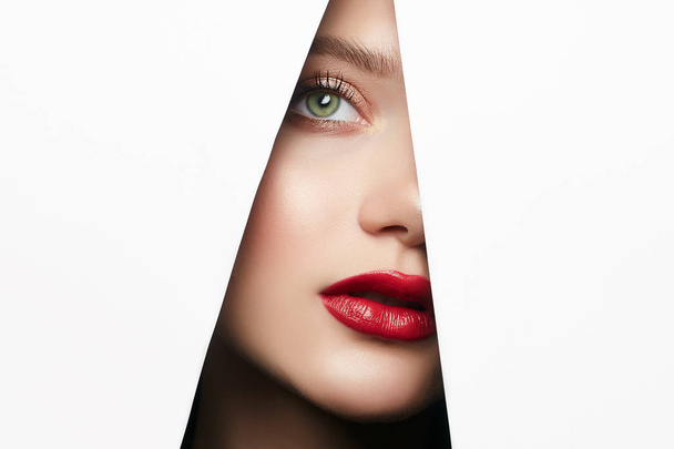 young beautiful woman with a bright makeup. make-up artist concept. A girl with beautiful bright green eyes, looks into the hole of white paper - Photo, Image