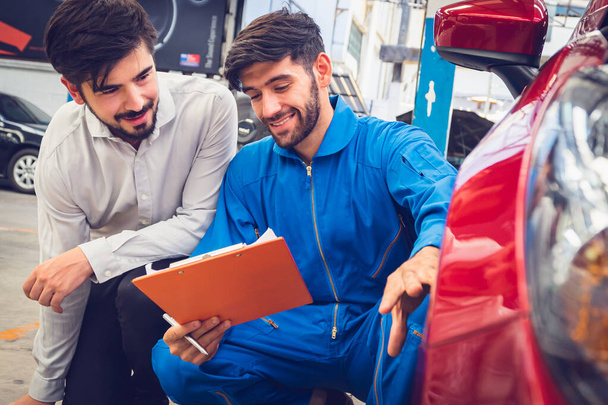 Mechanic holding clipboard with car owner in the workshop garage. Car auto services concepts - Photo, Image