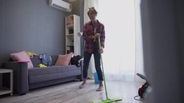 Happy young woman cute housewife is washing floor with mop and dancing at home - Filmagem, Vídeo