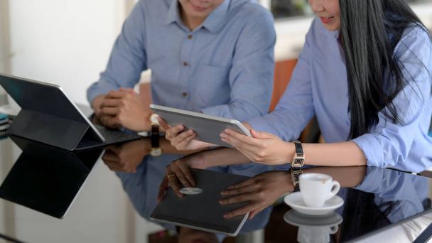 Ausschnitt von Geschäftsleuten, die sich auf ihre Arbeit mit digitalen Tablets am schwarzen Schreibtisch im Co-Working Space konzentrieren - Foto, Bild