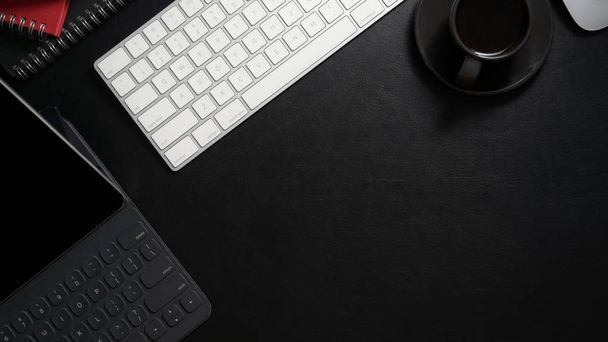 Widok góry ciemnego nowoczesnego miejsca pracy z tabletem cyfrowym, klawiaturą komputera, filiżanką kawy i przestrzenią do kopiowania na czarnym stole - Zdjęcie, obraz