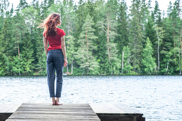 Young girl standing on the pier of a beautiful lake, looking away. Summer mood, the joy of the beauty of nature, summer. The concept of the future    - Foto, afbeelding