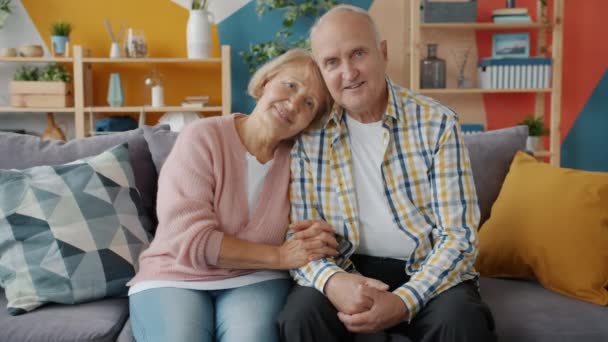 Portrait of couple senior man and woman smiling looking at camera at home on sofa - Filmati, video