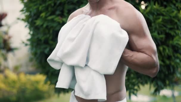 chlap otírá nahý trup s bílým ručníkem v blízkosti krásných stromů - Záběry, video
