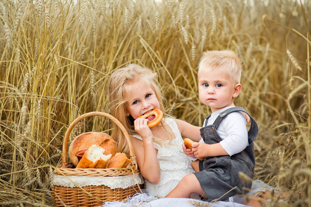 chłopiec i dziewczyna na pikniku na polu pszenicy jedzący wypieki - Zdjęcie, obraz