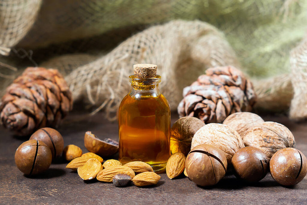 Natural Serums. Cosmetic and medicinal oil of macadamia, almonds, walnuts, pine nuts on a brown background, close-up. oil for women, cosmetology, treatment - Φωτογραφία, εικόνα