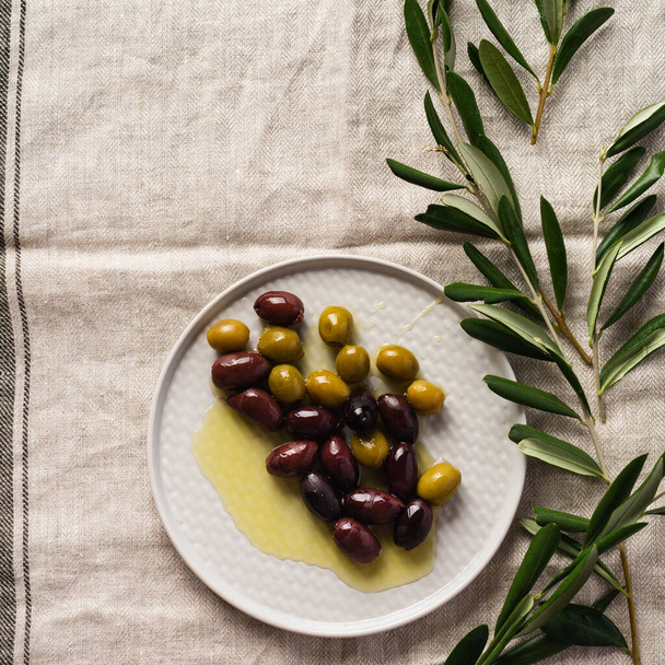Several varieties of fresh olives in different ceramic plates on an old vintage gray napkin tablecloth table background. Natural product concept. Rustic vintage set of cutlery. Top view, copy space. - Zdjęcie, obraz