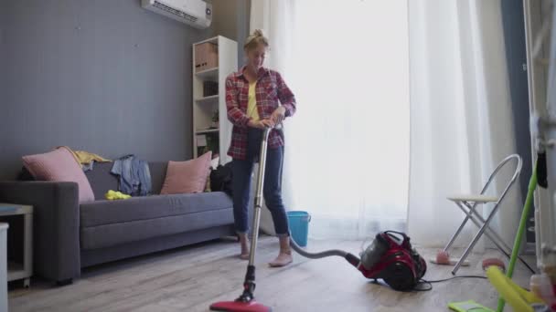 Woman using vacuum cleaner listen to music and dancing - Záběry, video
