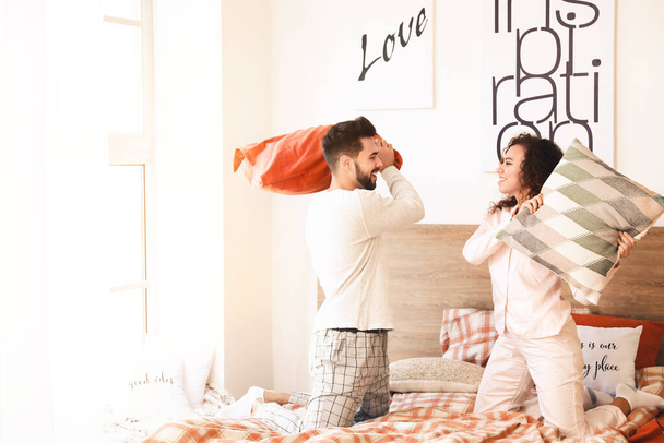 Happy young couple fighting on pillows in bedroom - Photo, Image
