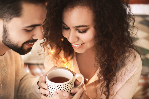 Happy young couple with cup of tea in bedroom - Fotoğraf, Görsel