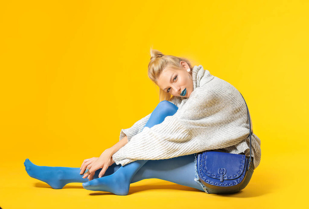 Молода жінка з креативним макіяжем і теплим светром на кольоровому фоні
 - Фото, зображення