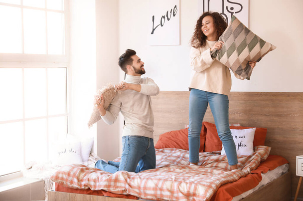 Happy young couple fighting on pillows in bedroom - Photo, image