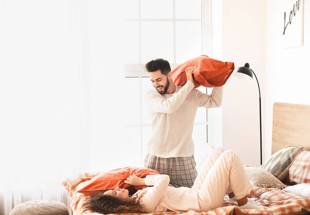 Feliz joven pareja luchando sobre almohadas en el dormitorio
 - Foto, imagen