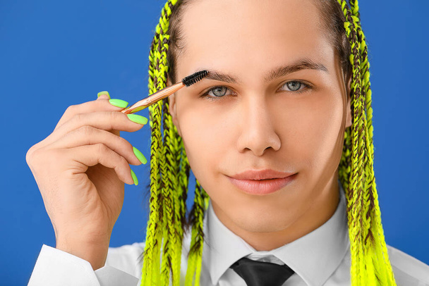 Mujer transgénero aplicando maquillaje contra el fondo de color
 - Foto, Imagen