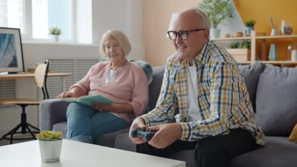Slow motion of happy senior couple playing video game and reading book at home - Filmmaterial, Video