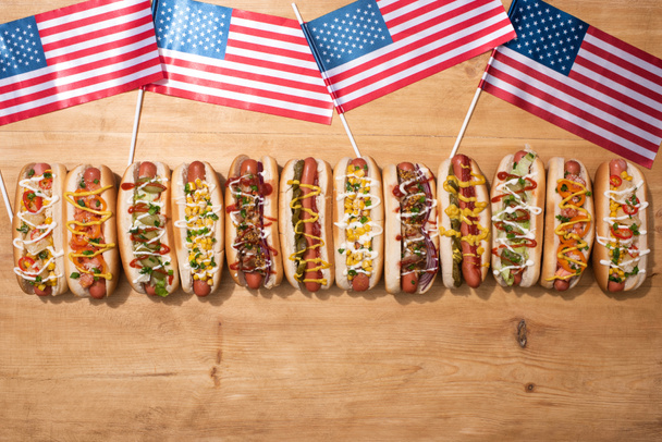 vrchní pohled na čerstvé lahodné hot dogy a americké vlajky na dřevěném stole - Fotografie, Obrázek